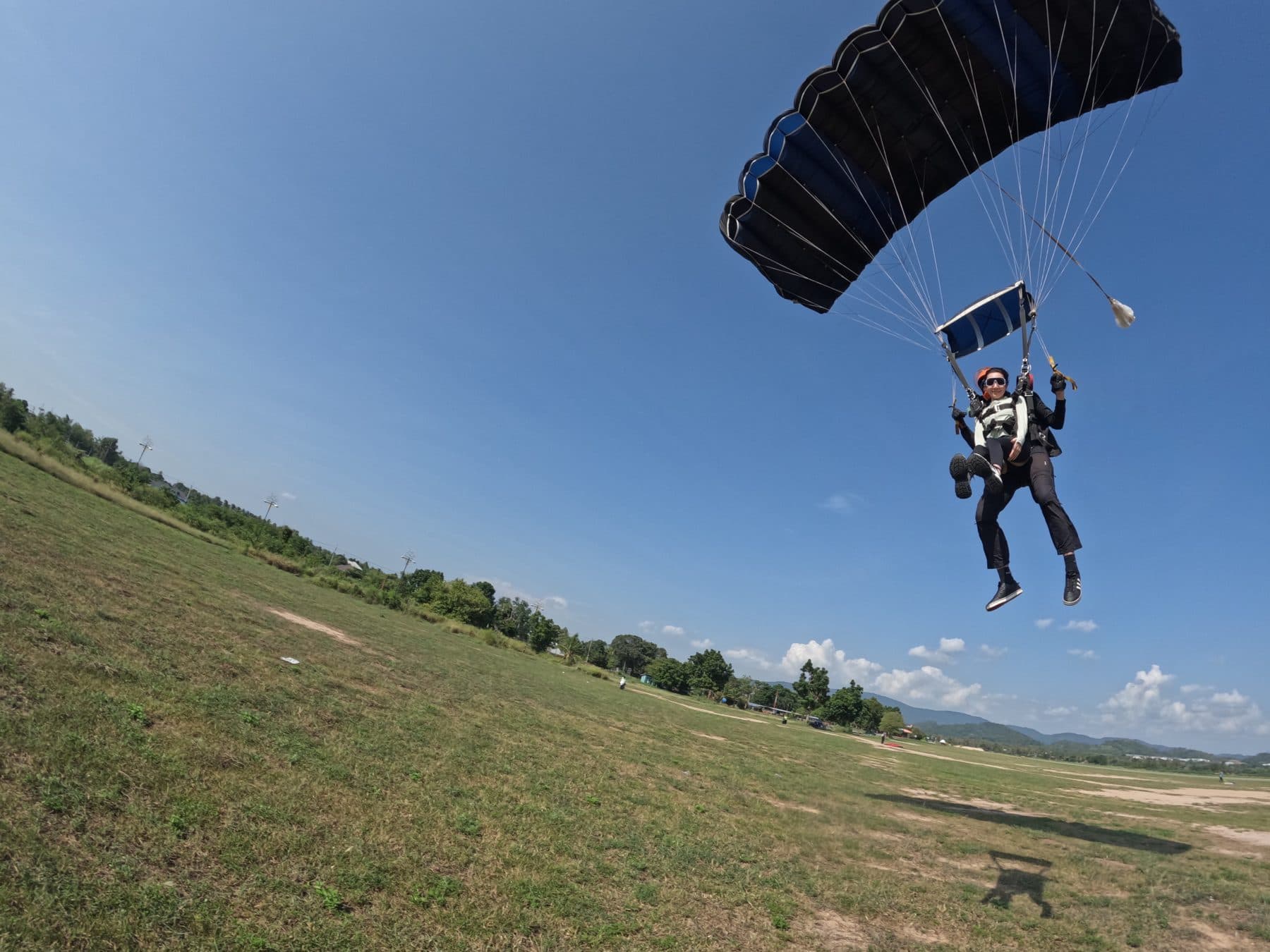 Tandem pair gliding in under an open parachute above the landing field